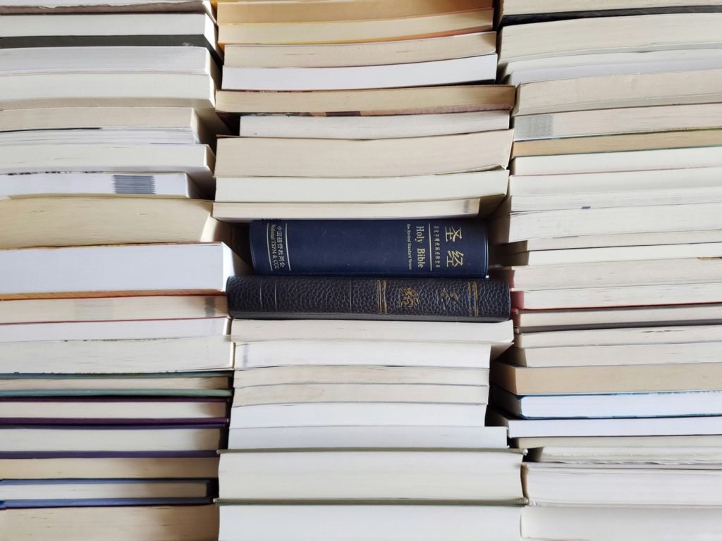 A collection of stacked books with visible Holy Bibles in a library arrangement.
