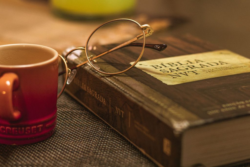 A Biblia Sagrada with glasses rests on a table beside a red mug, symbolizing relaxation and reflection.