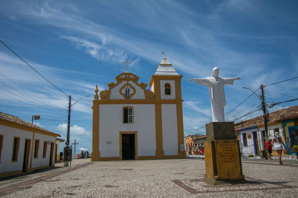 Scenic view of a historic church and Christ statue in a sunny Brazilian square.