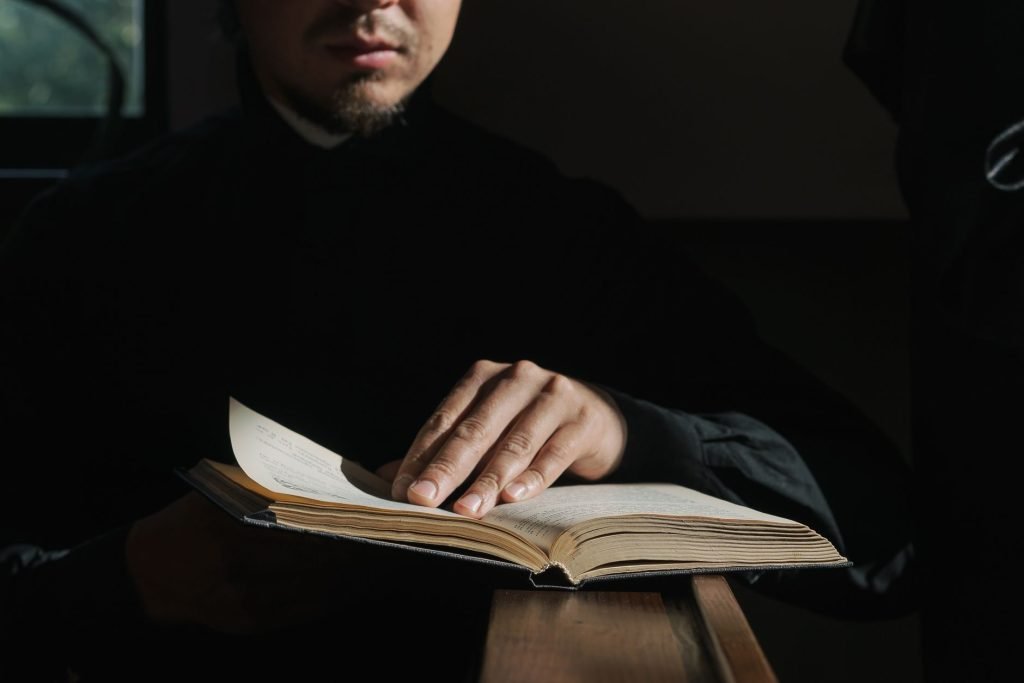 A man in dark clothing reads a Bible in a dimly lit church, highlighting faith and reflection.