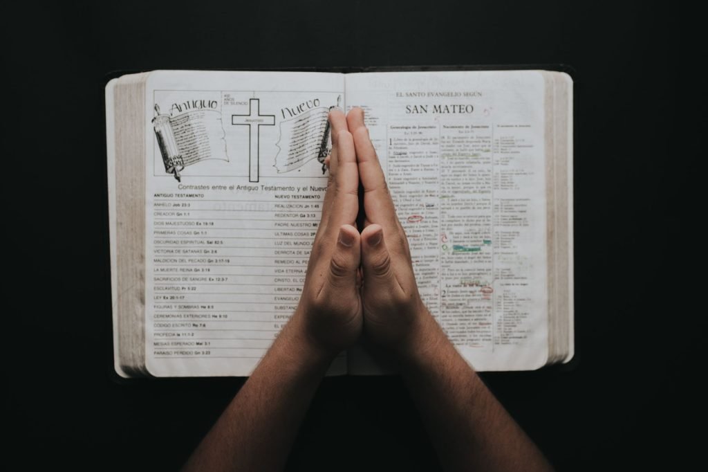 Hands clasped in prayer on an open Bible showing the book of Matthew, emphasizing faith and spirituality.