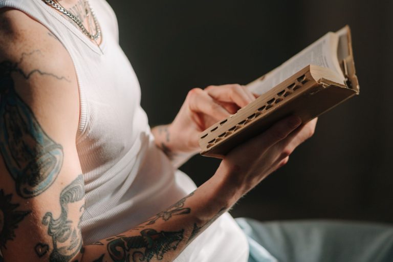 Close-up of a tattooed person reading a book, highlighting faith and focus.