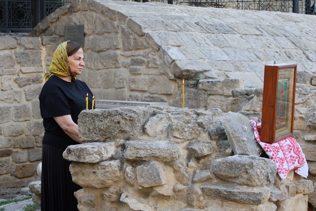 A woman in a headscarf and candles beside religious icon at historic stone ruins. Reflective moment.