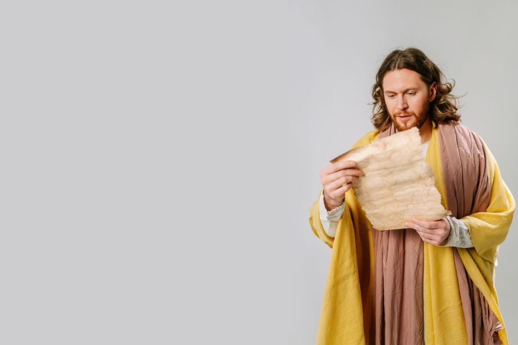 A man dressed in traditional robes holds an ancient parchment in a studio setting.