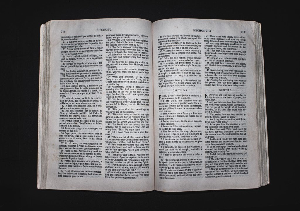 An open Bible displaying chapters of Acts in Spanish and English, photographed from above.