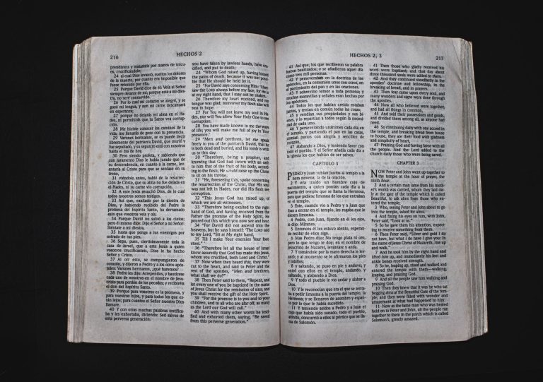 An open Bible displaying chapters of Acts in Spanish and English, photographed from above.
