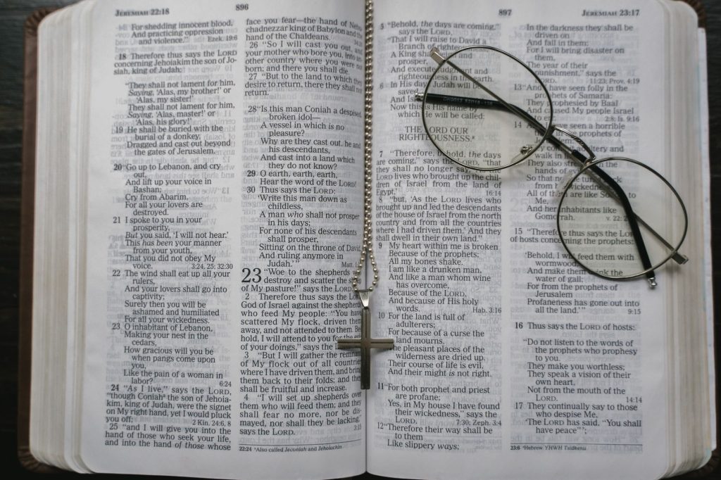 Close-up of an open Bible with a cross necklace and eyeglasses resting on the pages.