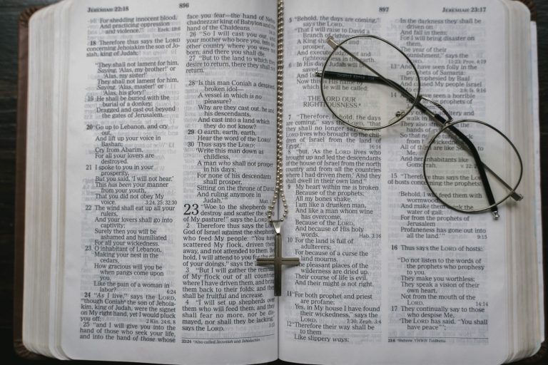 Close-up of an open Bible with a cross necklace and eyeglasses resting on the pages.