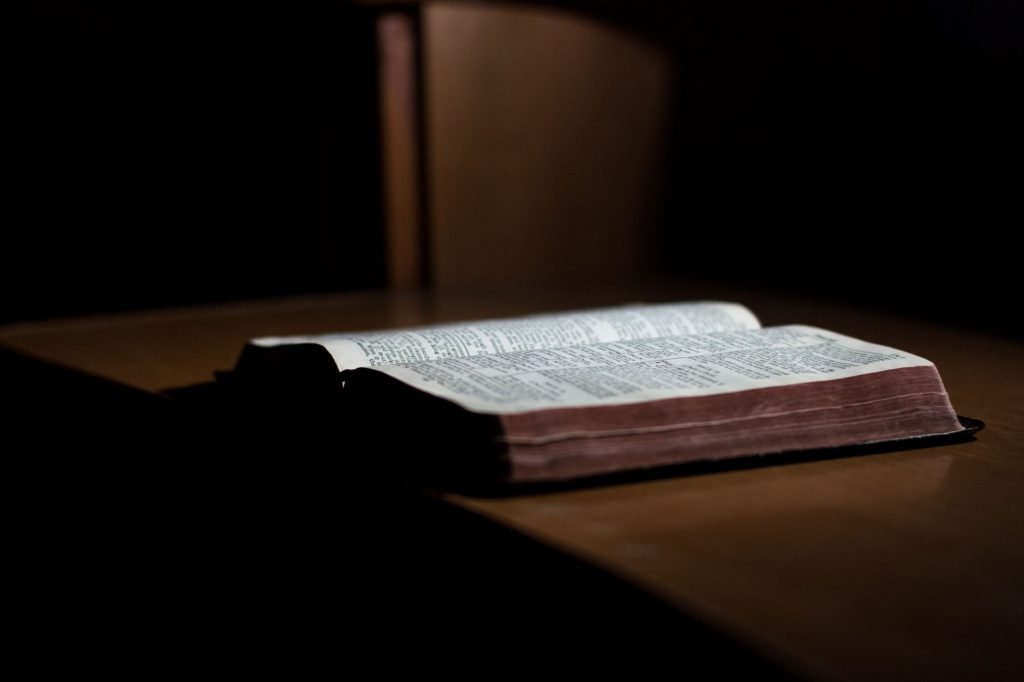 A dimly lit open Bible rests on a wooden table, inviting reflection and study.