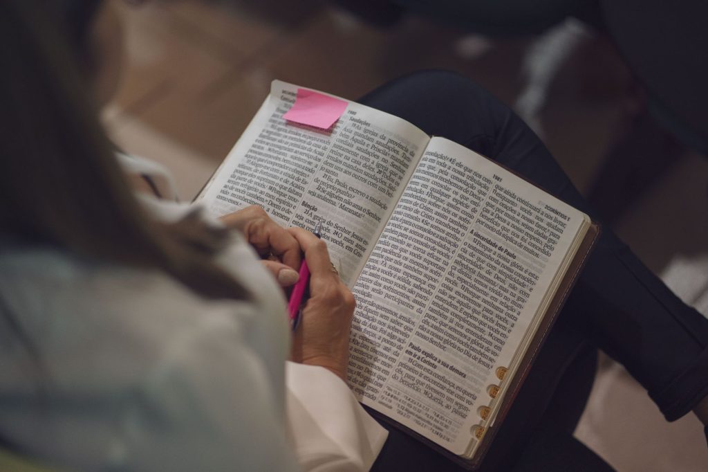 A woman reading a Bible with a pink note, captured indoors showing devotion and study.