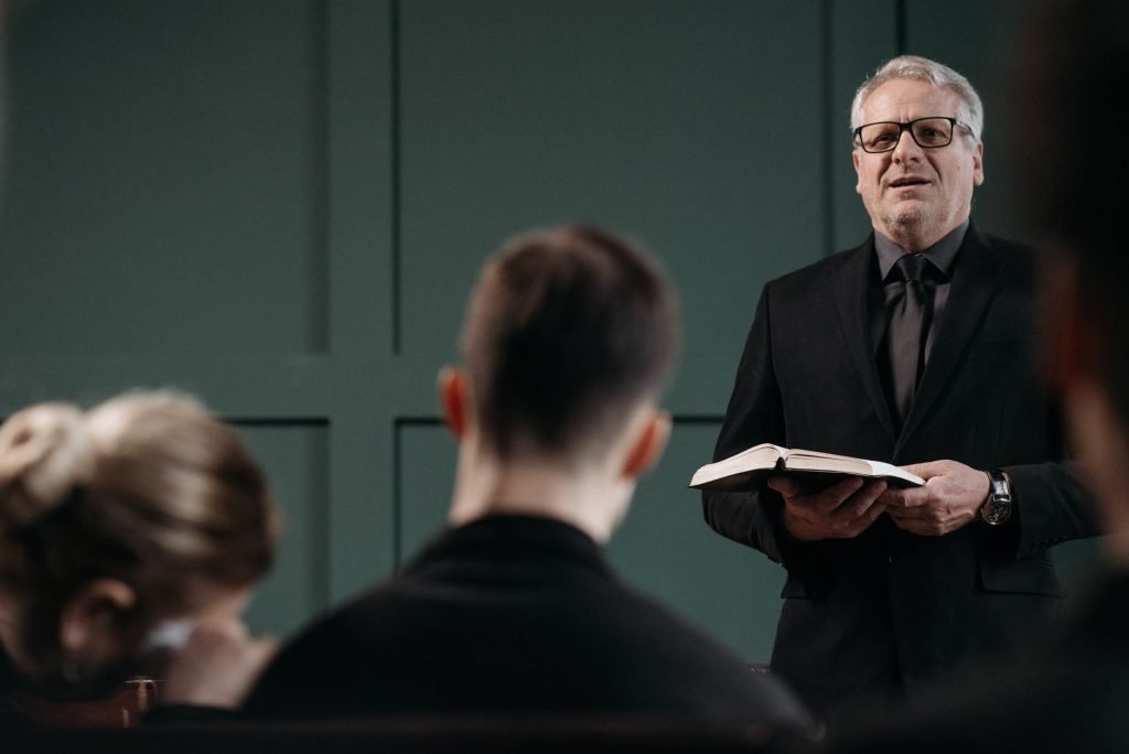 A pastor conducts a respectful funeral ceremony indoors, conveying solemnity and empathy.
