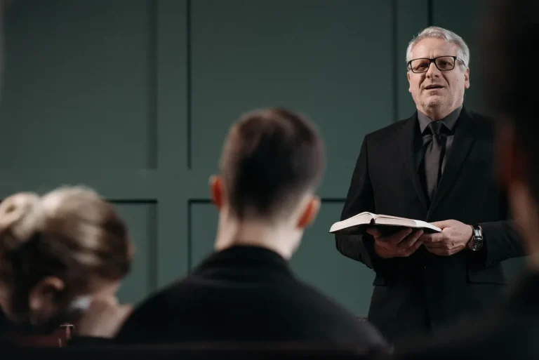 A pastor conducts a respectful funeral ceremony indoors, conveying solemnity and empathy.