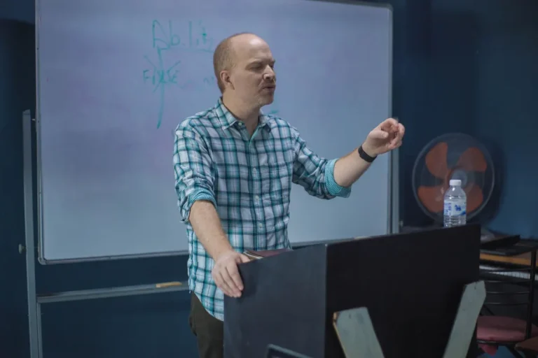 Male lecturer presenting a concept during a university lecture with a whiteboard in the background.
