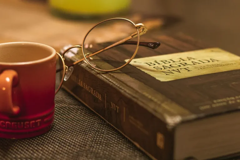 A Biblia Sagrada with glasses rests on a table beside a red mug, symbolizing relaxation and reflection.