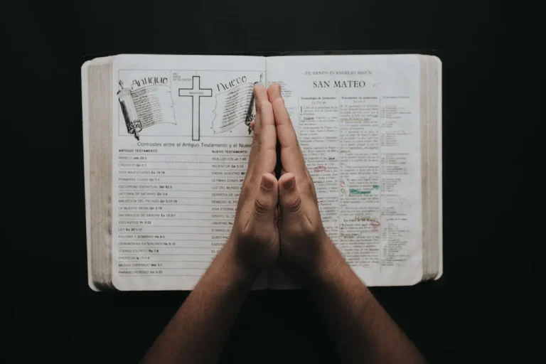 Hands clasped in prayer on an open Bible showing the book of Matthew, emphasizing faith and spirituality.