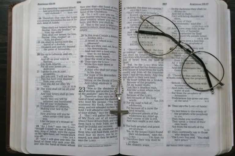 Close-up of an open Bible with a cross necklace and eyeglasses resting on the pages.