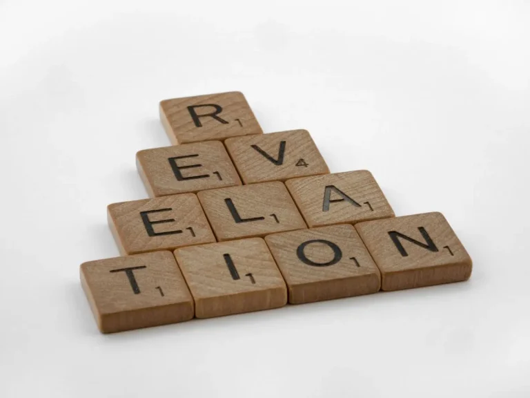 Wooden Scrabble tiles arranged to spell 'Revelation' on a white background, ideal for educational themes.
